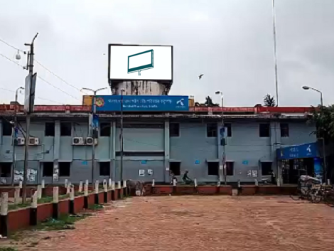 A large, vibrant digital billboard at the Barishal Launch Terminal entry gate displaying an advertisement, with clear, high-quality visuals and a bustling terminal scene in the background.